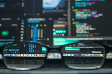 Eyeglasses reflecting computer code on a monitor, ideal for technology and programming themes.